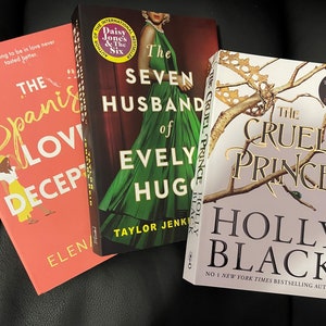 Puede incluir: Tres libros de bolsillo apilados uno encima del otro. El libro de arriba es blanco con letras doradas y el título "The Cruel Prince" de Holly Black. El libro del medio es verde con letras blancas y el título "The Seven Husbands of Evelyn Hugo" de Taylor Jenkins Reid. El libro de abajo es rosa con letras amarillas y el título "The Spanish Love Deception" de Elena Armas.
