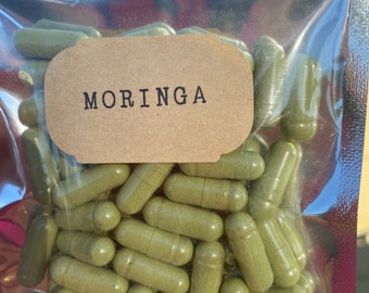 May include: A clear plastic bag filled with green capsules labeled "MORINGA".