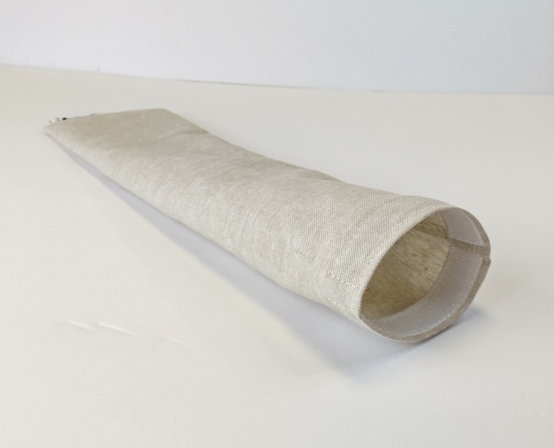 Op de afbeelding: Een beige linnen bestekhouder met een witte naad rond de opening.