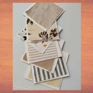 May include: A collection of square fabric swatches featuring various patterns and textures, including solid beige, cream, white and beige stripes, black and white ticking stripes, and a cream fabric with a brown botanical floral print.