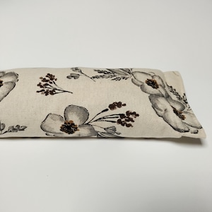 Op de afbeelding: Een wit oogkussen met een bloemenpatroon met grijze en bruine bloemen. Het kussen is gemaakt van een zachte, natuurlijke stof.