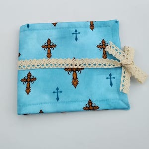 May include: A blue fabric pouch with a white lace trim and a brown cross pattern. The pouch is tied with a white lace ribbon.