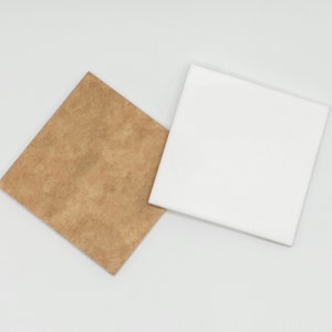 May include: Two square pieces of fabric, one brown and one white, are lying on a white surface.