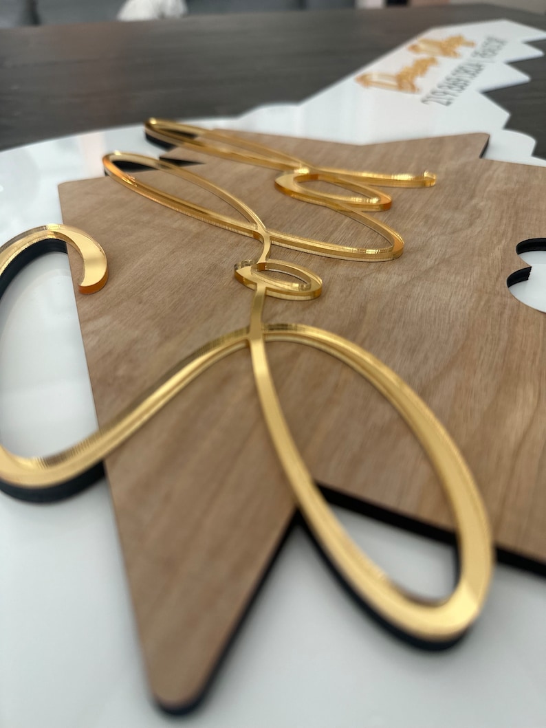 May include: A wooden sign with the word "Sofia" written in gold cursive lettering. The sign is shaped like a star and has a black border.