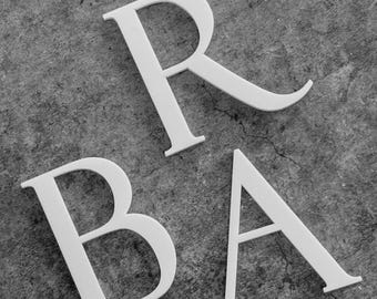 May include: White capital letters 'R', 'B', and 'A' are arranged on a textured gray surface. The letters are sans-serif and appear to be made of a solid material, casting subtle shadows.
