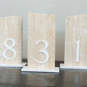 Pu&ograve; includere: Tre portanumero da tavolo rettangolari. Ognuno &egrave; di colore beige chiaro con un numero bianco: 8, 3 e 1. I numeri sono attaccati alla parte anteriore della pietra beige. Ogni portanumero &egrave; su una base bianca.