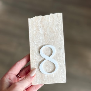 Pu&ograve; includere: Una piastrella rettangolare in pietra beige chiaro con il numero otto bianco attaccato. La piastrella ha una superficie ruvida e strutturata. Il numero otto &egrave; in un carattere corsivo.