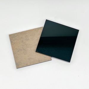 May include: Two square pieces of material, one black and one brown, are lying on a white surface. The black piece is smooth and glossy, while the brown piece is textured.