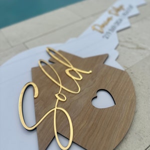 May include: A white and wood house-shaped sign with the word "Sold" written in gold script. The sign has a heart cut out of the wood.