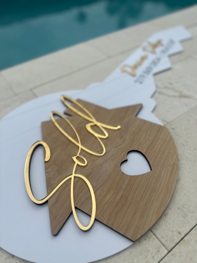 May include: A white and wood house-shaped sign with the word "Sold" written in gold script. The sign has a heart cut out of the wood.