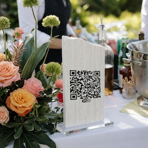 May include: A rectangular, light-colored stone sign with a rough, natural edge features a black printed QR code and the text Wi-Fi below it. The sign is mounted on a clear, rectangular acrylic base, standing upright on a white surface.