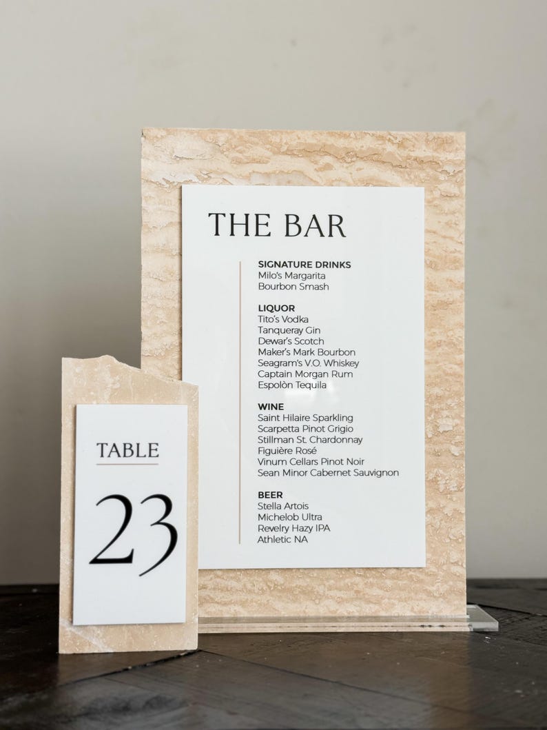 May include: A bar menu and table number 23 are displayed. The bar menu lists signature drinks, liquor, wine, and beer options. The table number is on a separate card. Both cards have a textured, beige background.