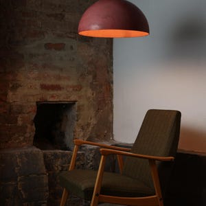 Pu&ograve; includere: Una poltrona marrone con gambe in legno si trova in una stanza con un muro di mattoni e un camino. Un lampadario a cupola rosa &egrave; appeso al soffitto.