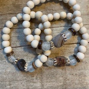 May include: Three white wooden bead bracelets with brown and clear glass beads and agate stones.