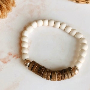 May include: A white and brown beaded bracelet with a silver accent. The bracelet is made of wooden beads and has a simple design.