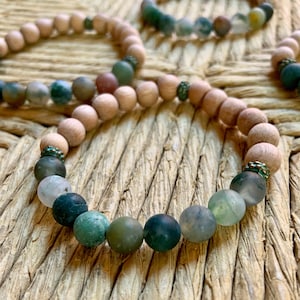 May include: A wooden beaded bracelet with green agate stones. The bracelet has a natural wood color and features a gradient of green agate stones.