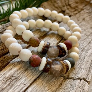 May include: Two bracelets made of white beads with brown, red, and clear beads. The bracelets are on a wooden surface.
