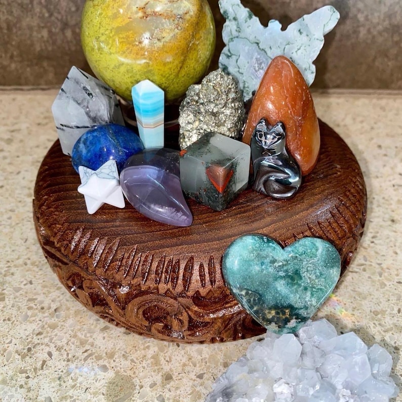 May include: A wooden display stand with a variety of crystals and stones, including a green heart-shaped stone, a black cat figurine, and a clear quartz crystal.