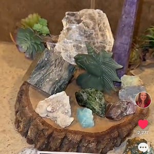 May include: A wooden display stand with a variety of crystals and stones, including a clear selenite, a purple amethyst, a green jade dragon, and a variety of other stones. The stand is labeled "Woo Woo Wellness Writer $144.44 Intuitive Crystal Set".