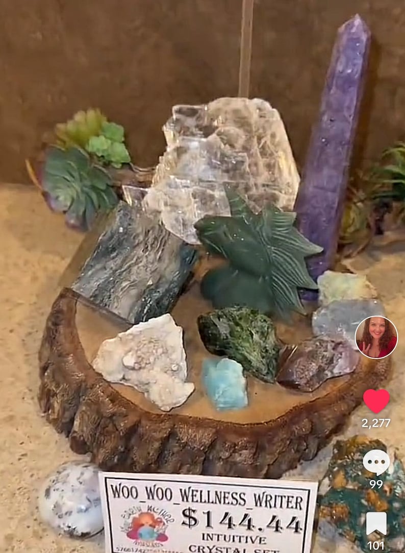 May include: A wooden display stand with a variety of crystals and stones, including a clear selenite, a purple amethyst, a green jade dragon, and a variety of other stones. The stand is labeled "Woo Woo Wellness Writer $144.44 Intuitive Crystal Set".