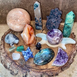 May include: A collection of polished crystals and stones, including a large orange carnelian, a green aventurine, a purple amethyst, a blue labradorite, a green jade, a pink rose quartz, a grey turtle, a blue star, a hamsa hand, and a white moon.