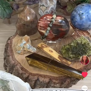May include: A collection of crystals and stones on a wooden display stand. The set includes a large red and brown crystal, a smaller brown crystal, a green crystal, a blue crystal, a yellow crystal, and a clear crystal. The crystals are arranged in a circle on the stand. The stand is made of wood and has a natural finish. The crystals are all different shapes and sizes. The set is priced at $99.99 and is called "Intuitive Crystal Set".