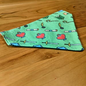 Może przedstawiać: Zielona bandana z powtarzającym się wzorem mieczy, serc, zwojów i piór.