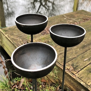 Large rain catchers made of metal which rust over time,  can be filled with water, birds drawn to bathe, jetty and pond in background