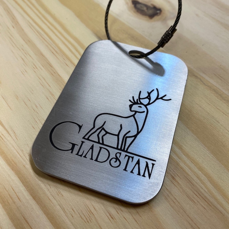 May include: Silver luggage tag with a black engraved deer and the text "GLADSTAN".