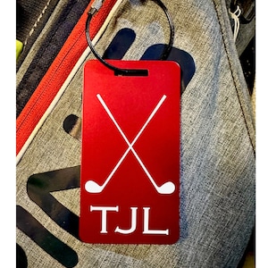 May include: Red luggage tag with a white golf club design and the initials "TJL" printed in white.