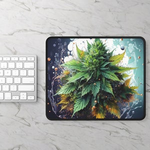 May include: A rectangular mouse pad featuring a vibrant green cannabis plant illustration centered against a dark blue and white background with abstract liquid splashes, bubbles, and small orange spheres, finished with a black stitched edge.