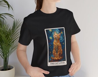 May include: Black t-shirt featuring a graphic of a cat sitting in a starry night sky. The graphic is within a rectangular frame with the text "THE CAT LOVER" at the bottom.