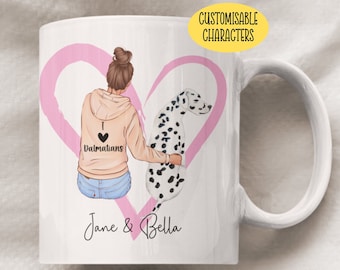 May include: White ceramic mug with a pink heart design. The heart features a cartoon illustration of a woman with brown hair wearing a light brown hoodie with the text "I love Dalmatians" and a dalmatian dog. The text "Jane & Bella" is printed below the heart.