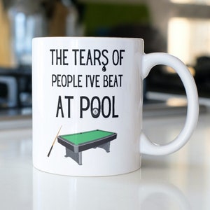 May include: White ceramic mug with a black design that says "The Tears of People I've Beat At Pool" with a cartoon image of a pool table and cue stick.