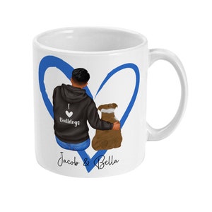 May include: White ceramic mug with a blue heart design. The heart features a cartoon illustration of a person with a dog. The person is wearing a black hoodie with the text "I love Bulldogs" on it. The text "Jacob & Bella" is written below the heart.