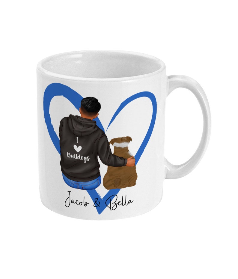 May include: White ceramic mug with a blue heart design. The heart features a cartoon illustration of a person with a dog. The person is wearing a black hoodie with the text "I love Bulldogs" on it. The text "Jacob & Bella" is written below the heart.