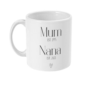 Puede incluir: Taza de cer&aacute;mica blanca con asa curva. La taza presenta las palabras "Mum EST. 1995" encima de "Nana EST. 2021" y un peque&ntilde;o s&iacute;mbolo de coraz&oacute;n. La taza est&aacute; dise&ntilde;ada para una madre y una abuela.