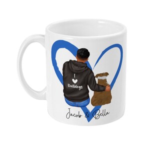 May include: White ceramic mug with a blue heart design. The heart is drawn around a man and a dog. The man is wearing a black hoodie with the text "I love Bulldogs" on it. The text "Jacob & Bella" is written below the heart.