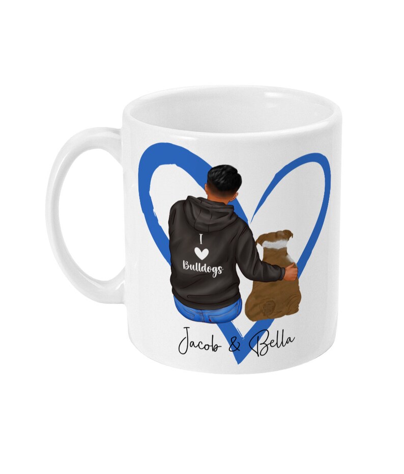 May include: White ceramic mug with a blue heart design. The heart is drawn around a man and a dog. The man is wearing a black hoodie with the text "I love Bulldogs" on it. The text "Jacob & Bella" is written below the heart.