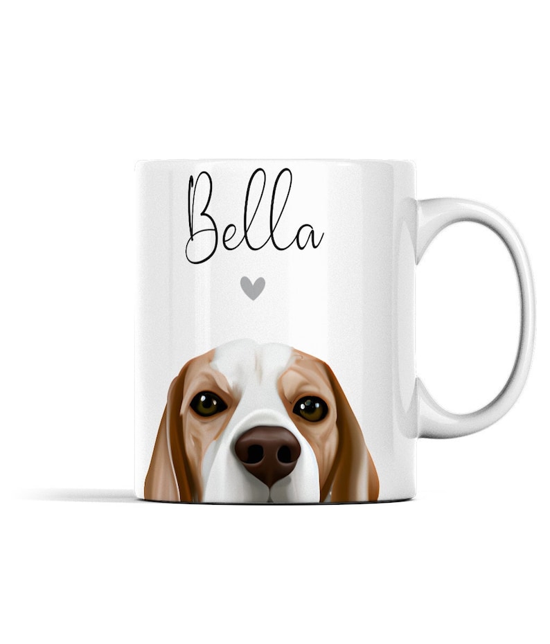 Puede incluir: Taza de cer&aacute;mica blanca con un beagle marr&oacute;n y blanco asom&aacute;ndose por el borde. La taza tiene el nombre "Bella" escrito en cursiva negra con un peque&ntilde;o coraz&oacute;n gris arriba.