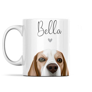 Puede incluir: Taza de cer&aacute;mica blanca con una ilustraci&oacute;n de un perro beagle marr&oacute;n y blanco. La cabeza del perro asoma por el borde de la taza. El texto "Bella" est&aacute; impreso en la taza en letra cursiva negra con un peque&ntilde;o coraz&oacute;n gris debajo del texto.