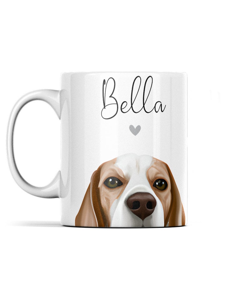 Puede incluir: Taza de cer&aacute;mica blanca con una ilustraci&oacute;n de un perro beagle marr&oacute;n y blanco. La cabeza del perro asoma por el borde de la taza. El texto "Bella" est&aacute; impreso en la taza en letra cursiva negra con un peque&ntilde;o coraz&oacute;n gris debajo del texto.