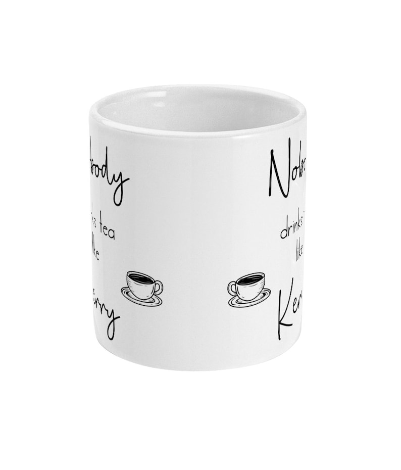 May include: White ceramic mug with black text that reads "Nobody drinks tea like Kerry" and "Nobody drinks tea like Kerry". The text is written in a cursive font. There are two black and white illustrations of coffee cups on the mug.