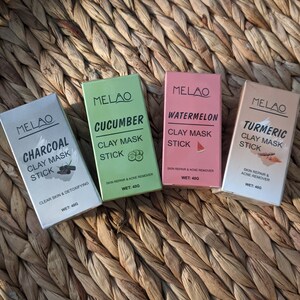 May include: Four clay mask sticks in individual boxes. The boxes are green, pink, white, and beige. The boxes are labeled with the brand name "MELAO" and the flavor of the mask stick. The flavors are "Charcoal", "Cucumber", "Watermelon", and "Turmeric". Each box has the text "Clay Mask Stick" and the weight of the product, "40g".