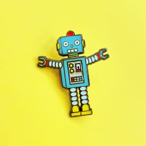 Puede incluir: Un pin de robot azul con detalles amarillos y rojos. El robot tiene dos brazos con manos, una cabeza con dos ojos y un cuerpo con un panel de botones.