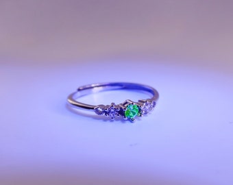 May include: A silver ring with a green gemstone and smaller clear gemstones.