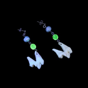 May include: A pair of earrings featuring a tooth charm, green and purple beads, and silver chain.