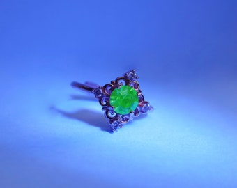 May include: A silver ring with a green gemstone and small clear stones set in a decorative design.