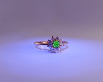 May include: A gold ring with a green gemstone surrounded by smaller clear gemstones.