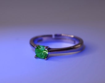 May include: A silver ring with a round, bright green gemstone. The ring has a simple band and a four-prong setting that holds the gemstone securely. The gemstone is the focal point of the ring.